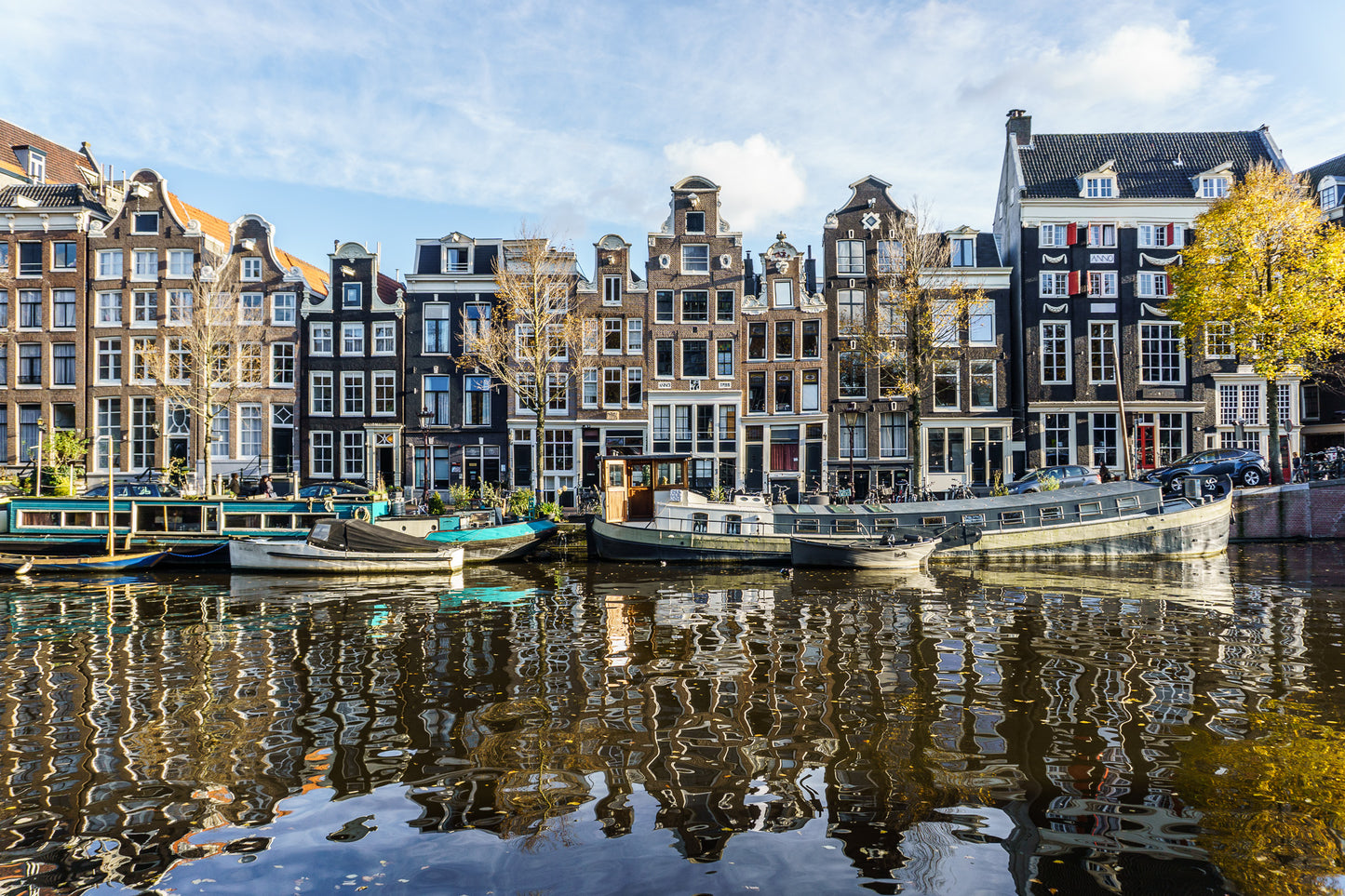 Casas tradicionales de Ámsterdam frente al canal con barcos amarrados y reflejos en el agua