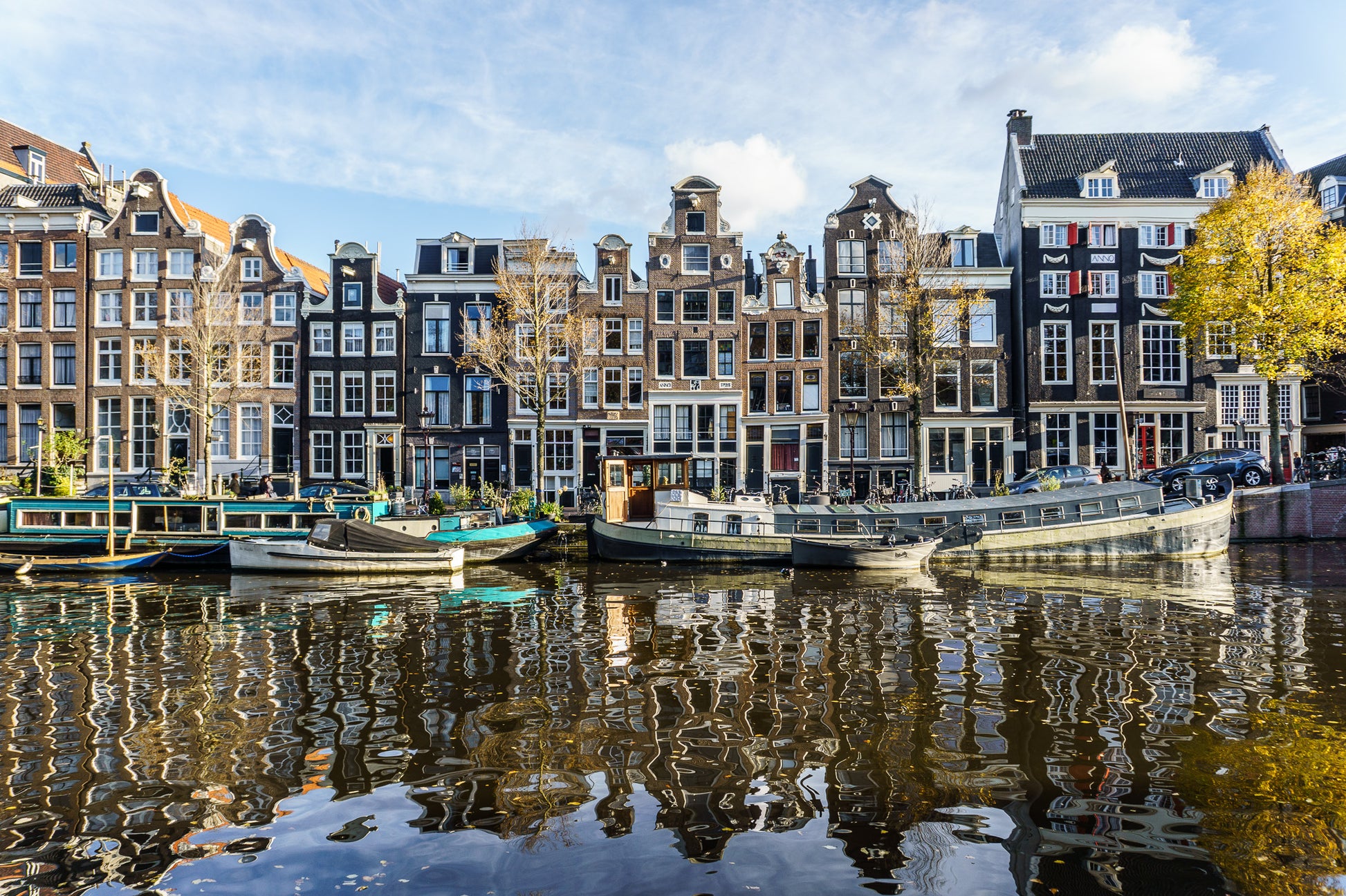 Casas tradicionales de Ámsterdam frente al canal con barcos amarrados y reflejos en el agua