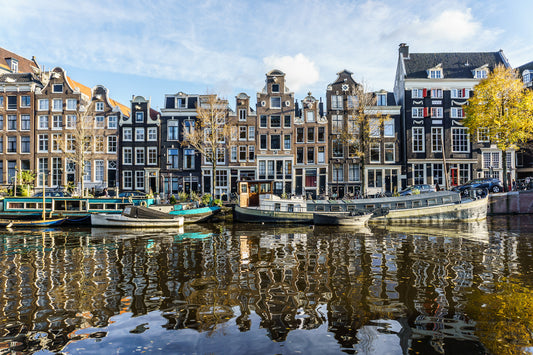 Casas tradicionales de Ámsterdam frente al canal con barcos amarrados y reflejos en el agua