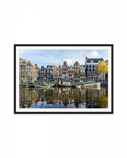 Casas tradicionales de Ámsterdam frente al canal con barcos amarrados y reflejos en el agua
