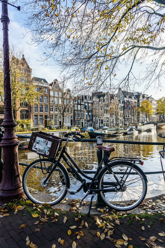 Bicicleta apoyada junto a un canal de Ámsterdam en otoño, con edificios clásicos y reflejos en el agua.