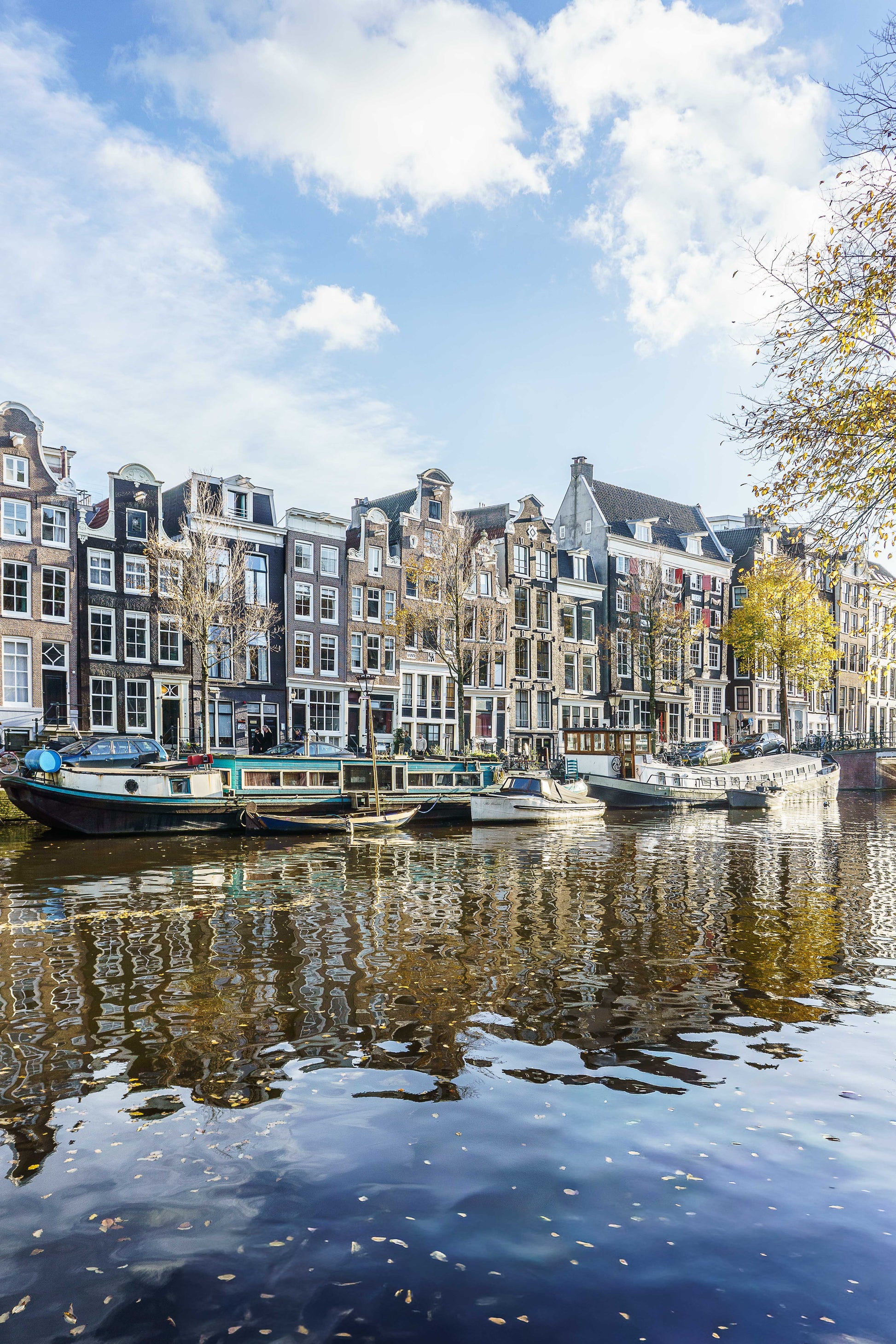 Canal de Ámsterdam en otoño con casas tradicionales, barcas y reflejos sobre el agua.
