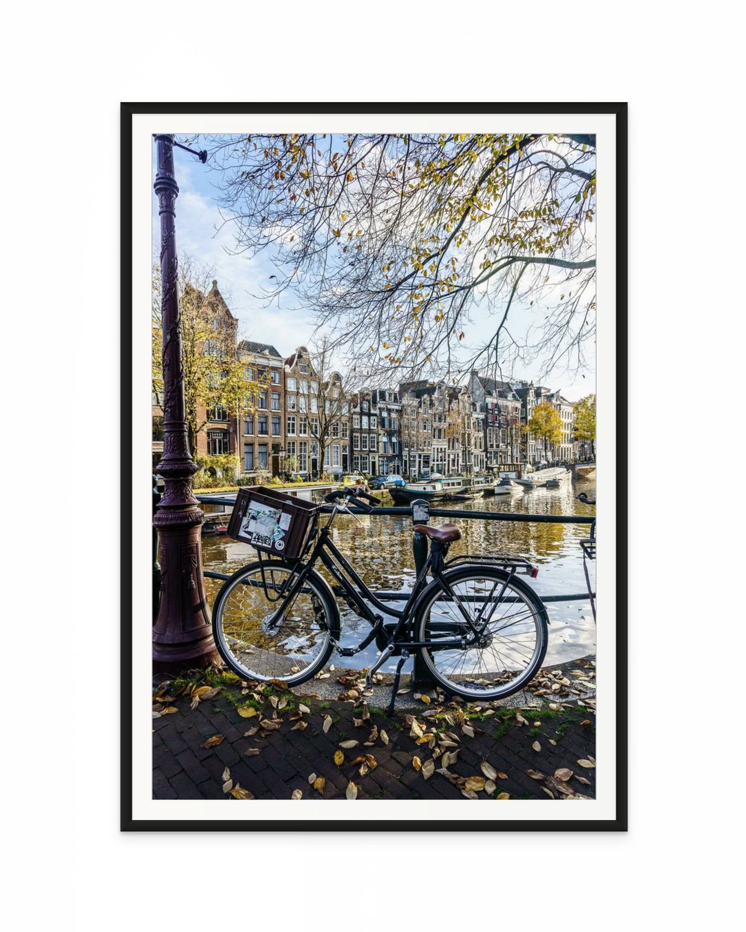 Bicicleta apoyada junto a un canal de Ámsterdam en otoño, con edificios clásicos y reflejos en el agua.
